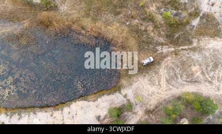 Aus der Vogelperspektive auf ein Auto, das in der Nähe eines kleinen Teichs in einer ländlichen Gegend parkt. Stockfoto