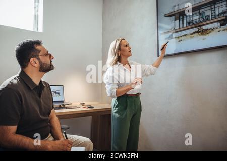 Eine Frau und ein Mann analysieren architektonische Entwurfskonzepte. Sie überprüfen digitale und physische Modelle moderner Gebäude und fördern Teamarbeit und Kreativität Stockfoto