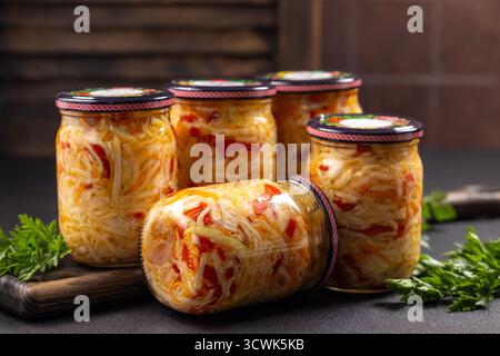 Glasgläser gefüllt mit hausgemachtem fermentiertem Kohl und rotem Pfeffersalat, die gesundes konserviertes Gemüse für die Winterlagerung und den Verzehr präsentieren Stockfoto
