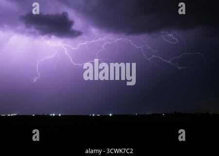 Ein mächtiger Gewitter erleuchtet den Nachthimmel mit hellen elektrischen Blitzen über einem fernen Horizont Stockfoto