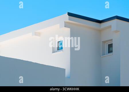 Modernes weißes minimalistisches Gebäude mit geometrischen Linien und Fenstern unter klarem blauem Himmel, zeitgenössische mediterrane Architektur. Selektiver Fokus Stockfoto