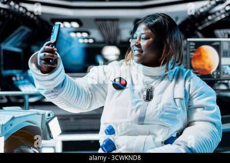 Glücklicher Astronaut, der mit seiner Familie Video macht, bevor er Raumschiff auf dem Mars landet. Frau, die ein Smartphone benutzt, mit ihren Lieben während der Mission auf der Oberfläche des roten Planeten spricht, um das Überleben der Menschen im Weltraum zu testen Stockfoto