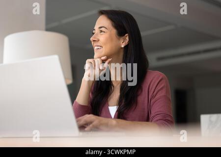 Glückliche, träumende, freischaffende Frau aus Lateinamerika, die am Computer arbeitet Stockfoto
