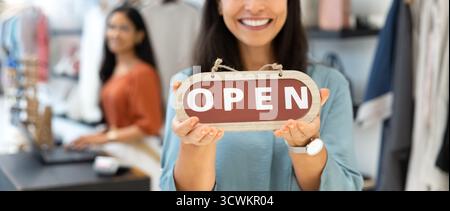 Friendly young small business owner woman holding Open sign Stockfoto