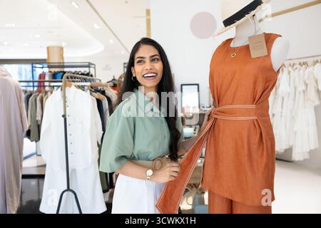 Fröhlicher indischer Ladenleiter, der Kleidung an Schaufensterpuppen anpasst Stockfoto
