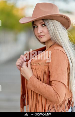 Porträt eines jungen weiblichen Models mit westlicher Mode, aufgenommen in warmem Licht während der goldenen Stunde vor rustikaler Kulisse. Stockfoto