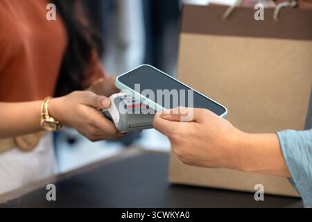 Zugeschnittene Aufnahme eines Boutique-Kunden, der den NFC-Service auf dem Handy nutzt Stockfoto