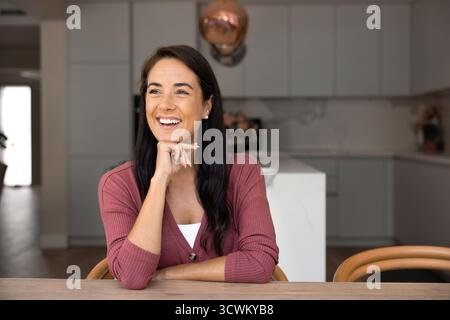 Fröhliche junge lateinische Hausbesitzerin, die am Tisch sitzt Stockfoto