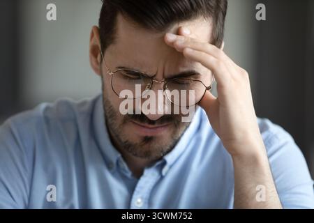Nahaufnahme trauriger Geschäftsmann, der mit geschlossenen Augen sitzt und an Kopfschmerzen leidet Stockfoto