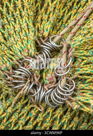 Nahaufnahme eines Abschnitts eines Meeresfischschleppnetzes mit verflochtenen Seilen in Gelb mit grünen Akzenten. Die Seile werden durch rostfreies Ross gefädelt Stockfoto