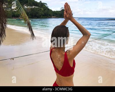 Nicht wiedererkennbare kaukasische Frau, die am tropischen Strand steht, mit Händen in einer Gebetsposition über dem Kopf als Geste namens Anjali Mudra. Stockfoto