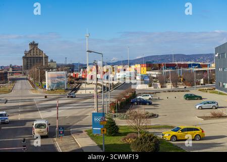 Der Csepel Freeport in Budapest, Ungarn, zeigt Eisenbahngleise, Frachtcontainer und Industriegebäude unter klarem Winterhimmel. Stockfoto