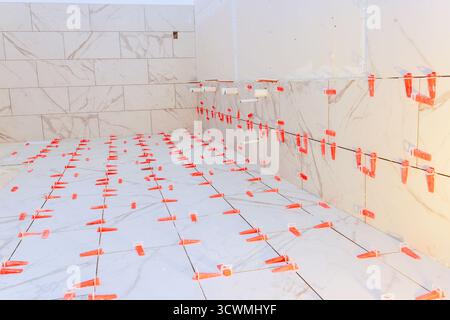 Die Arbeiter legen weiße Marmorfliesen auf den Boden und die Wand des Badezimmers und bereiten sich auf ein stilvolles Finish vor. Stockfoto