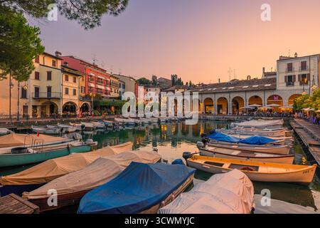 Lebendiger Sonnenuntergang über dem alten Hafen Porto Vecchio in Desenzano del Garda, Italien. Die belebten Terrassen und Restaurants am Wasser sind voll von Peop Stockfoto