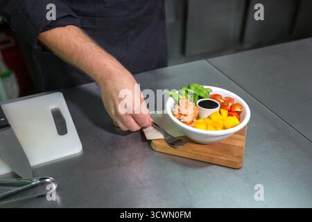 Nicht wiedererkennbarer Koch, der eine Gabel neben eine frische, bunte Poke-Schüssel mit Lachs in der Küche des Restaurants platziert Stockfoto