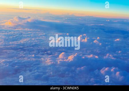 Atemberaubender Blick aus der Vogelperspektive fängt einen weiten Bereich flauschiger weißer Wolken ein, die im goldenen Sonnenuntergang vor blauem Himmel leuchten. Schichten von Kumulusformationen dehnen sich Stockfoto