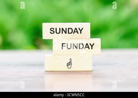 Holzblöcke sind gestapelt und mit SUNDAY FUNDAY bedruckt. Die nach oben zeigende Handgrafik sorgt für einen verspielten Ausdruck, der Freude und Vergnügen fördert. Stockfoto
