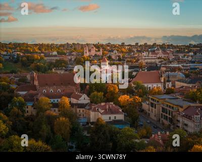 Blick aus der Vogelperspektive auf die Altstadt mit ihren Terrakotta-Dächern und barocken Kirchen inmitten eines Herbstgemäldes unter einem weichen, goldenen Himmel, Vilnius, Litauen. Stockfoto