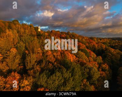 Aus der Vogelperspektive das Denkmal der drei Kreuze, das auf einem Hügel steht, der in lebhaften Herbstfarben unter einem dramatischen Himmel gekleidet ist, Vilnius, Litauen. Stockfoto