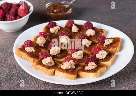 Kanapees mit Gänseleber, Feigendip und frischen Himbeeren auf weißem Teller Stockfoto