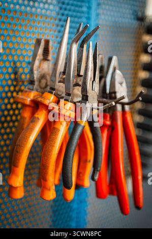 Zangen und verschiedene Handwerkzeuge hängen an einer Werkbankwand in einer Werkstattgarage Stockfoto