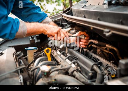 Hände eines Mechanikers, der Wartungsarbeiten am Motor des Fahrzeugs durchführt und Autoreparaturen anbietet Stockfoto