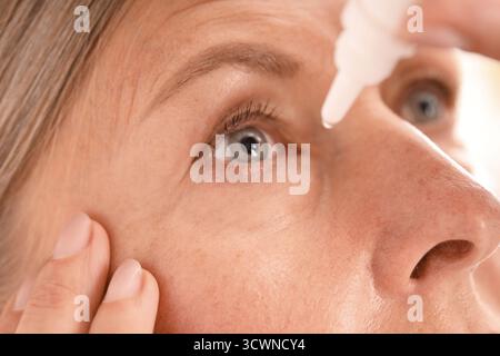 Frau, die Augentropfen auf hellem Hintergrund aufträgt, Nahaufnahme Stockfoto