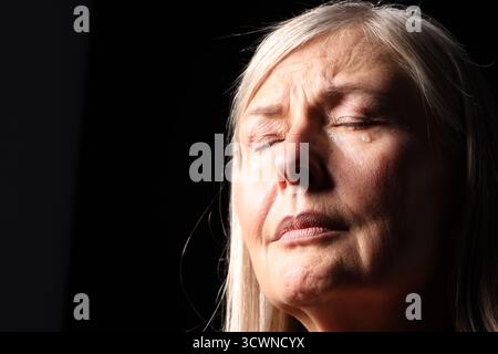 Ältere Frau weint auf schwarzem Hintergrund, Nahaufnahme. Leerzeichen für Text Stockfoto