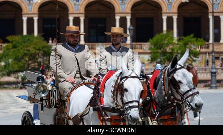 Sevilla, Spanien - 23. April: Zwei Männer in traditioneller Kleidung fahren auf einem sonnigen platz mit einer Pferdekutsche Stockfoto