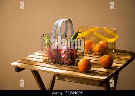 Frische Drachenfrüchte und Orangen in klaren Körben auf einem Holztisch, Obstkorb mit Drachenfrucht und Orangen auf Holztisch in der Küche Stockfoto