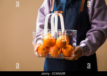 Eine Person, die einen klaren Korb frischer Orangen hält, eine Frau, die einen Korb Mandarinen in der Hand hält. Selektiver Fokus. Stockfoto