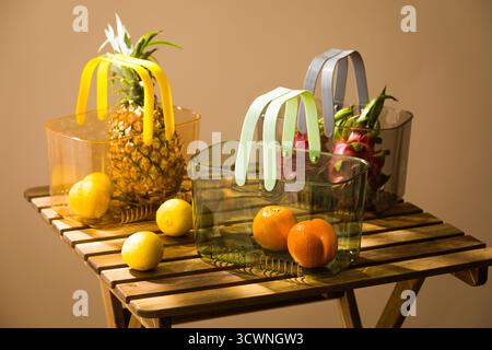 Bunte transparente Taschen gefüllt mit frischen Früchten auf einem Holztisch, Ananas, Zitrone, Ananas und anderen Früchten in einem Korb Stockfoto