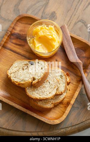Handwerkliche Brotscheiben mit goldener Butter und Holzstreuer auf einem rustikalen Tablett, Brotscheiben mit Butter auf Holzteller, Lebensmittelnähe Stockfoto
