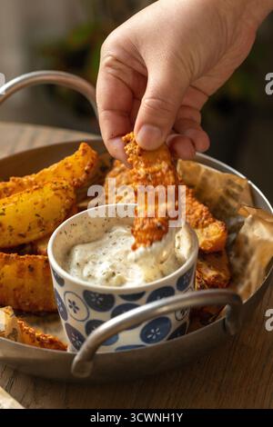 Würzigen Kartoffelkeil von Hand in einen cremigen Dip, Kartoffelfritten mit Sauerrahm und Mayonnaise in einer Schüssel tauchen Stockfoto