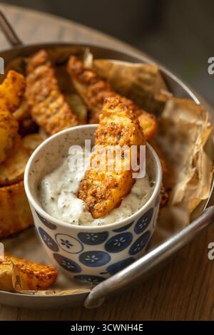 Knusprig gewürzte Kartoffelscheiben mit cremigem Kräuterdip, gebratene Kartoffelscheiben mit Tatarensauce. Selektiver Fokus Stockfoto