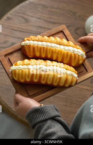Köstliche, cremegefüllte goldene Brötchen auf einem hölzernen Servierbrett, köstliche Eclairs mit Creme auf Holztablett, Nahaufnahme Stockfoto