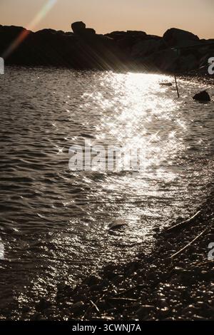 Sonnenlicht schimmert über die Meeresoberfläche und wirft einen glitzernden Pfad auf das Wasser. Die warmen Farbtöne der untergehenden Sonne schaffen eine friedliche und ruhige Atmosphäre Stockfoto