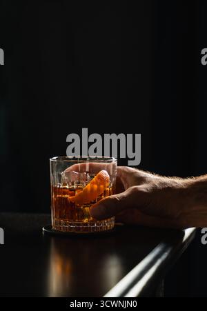 Die Hand des Mannes hält Cocktail in Whiskey-Glas auf schwarzem Hintergrund. Stockfoto