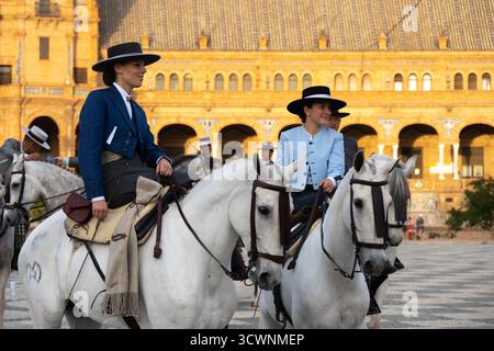 Sevilla, Spanien - 23. April: Zwei Frauen in traditioneller Kleidung reiten auf einem platz mit historischer Architektur im Hintergrund auf weißen Pferden Stockfoto