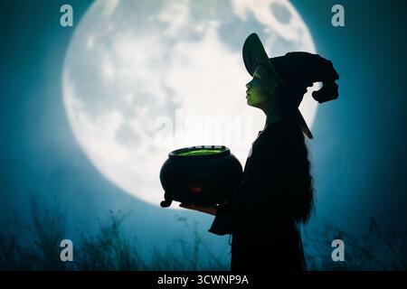 Mädchen in Hexenkostümen für Halloween. Junge, der auf Vollmond-Hintergrund steht. Stockfoto