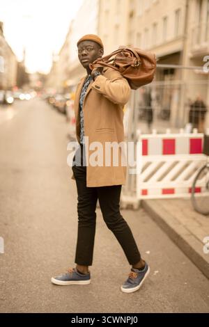 Rücksichtsvoller afrikanischer Mann, der mit der Tasche über der Schulter in der Stadt spaziert Stockfoto