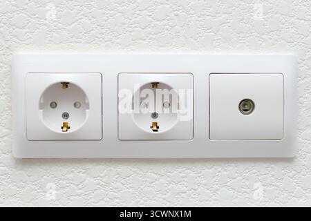 Weiße Steckdose mit zwei Steckdosen und TV-Kabelbuchse. Moderner Stromanschluss im Innenraum für die Hausverkabelung. Stockfoto