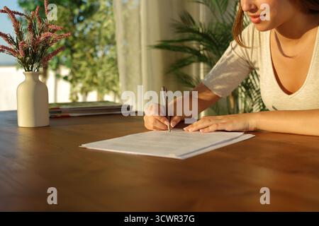 Nahaufnahme einer Frau, die ein Formular ausfüllt oder bei Sonnenuntergang zu Hause unterschreibt Stockfoto