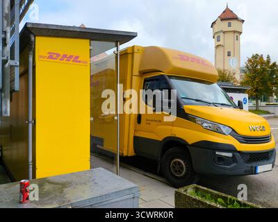 Gersthofen, Bayern, Deutschland - 7. Oktober 2025: Ein gelber DHL-Lieferwagen steht vor einer DHL-Packstation – ein Symbol für Paketzustellung, Versand und Auslieferung von Onlinebestellungen *** ein gelber DHL-Lieferwagen steht vor einer DHL-Packstation Symbol für Paketzustellung, Versand und Auslieferung von Onlinebestellungen Stockfoto
