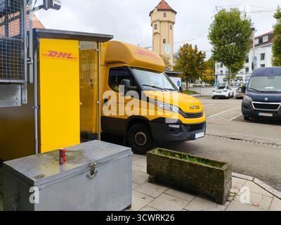 Gersthofen, Bayern, Deutschland - 7. Oktober 2025: Ein gelber DHL-Lieferwagen steht vor einer DHL-Packstation – ein Symbol für Paketzustellung, Versand und Auslieferung von Onlinebestellungen *** ein gelber DHL-Lieferwagen steht vor einer DHL-Packstation Symbol für Paketzustellung, Versand und Auslieferung von Onlinebestellungen Stockfoto