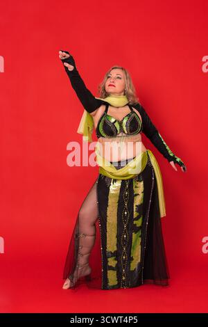Weibliche exotische Bauchtänzerin in schwarz-gelbem Tanzbühnen-Outfit – BH-Oberteil, Bolero und langer Rock mit Schlitz barfuß in voller Länge Stockfoto