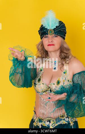 Erwachsene Frau mittleren Alters exotische Tänzerin, die in die Kamera schaut. Mode-Model-Kleid in gelb-grünem Ost-Tanzbühne Kostüm - Turban, BH-Top und SK Stockfoto