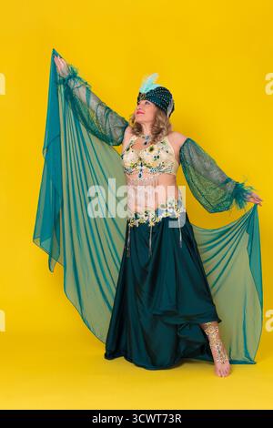 Reife Erwachsene Frau exotische Tänzerin mit handerhöhtem Anzug im grünen östlichen Tanzbühnenkostüm - Turban, BH-Top, Pareo und langer Rock mit Schlitz, Mo Stockfoto