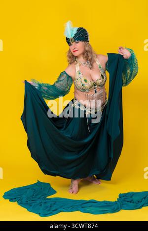 Mode-Model für Erwachsene mittleren Alters in grünem Outfit der östlichen Tanzbühne - Turban, BH-Oberteil und langer Rock mit Schlitz. Showgirl bewegt sich barfuß Stockfoto