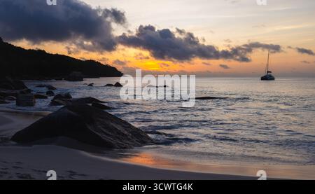 Eine ruhige Sonnenuntergangsszene über einer ruhigen Küste mit warmem orangefarbenem Licht, das auf sanften Wellen reflektiert. Landschaft von Anse Lazio, einem Strand in Stockfoto